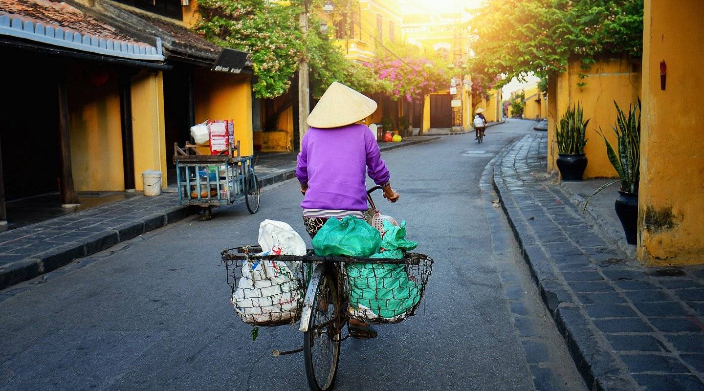 Woman cycling through the yellow streets of Hoi An old town, Vietnam
